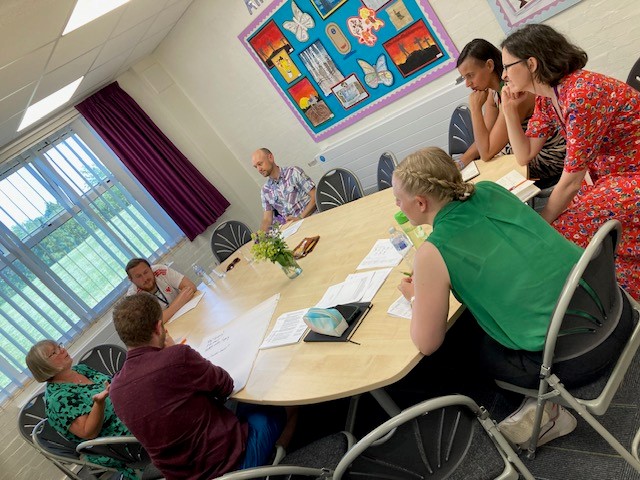 Teachers at a school, sat at a table discussing how to create action plans with trainers. 