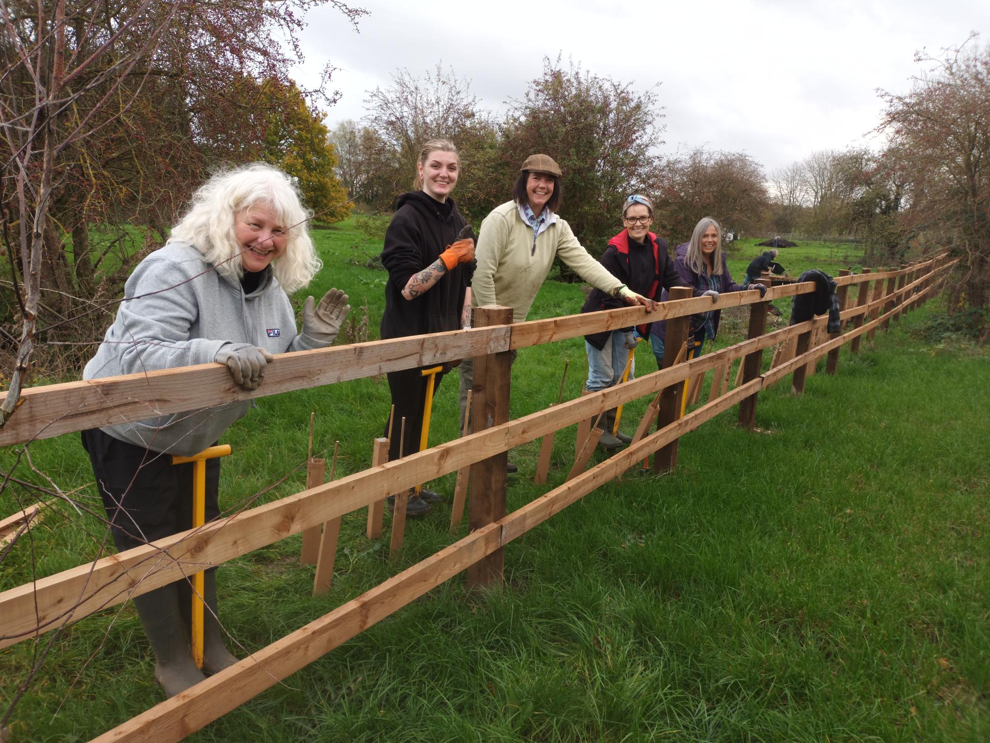 Image of 5 volunteers leaning against a fence on a field 