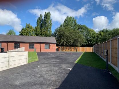 A photo of a new brick building with a grass area and new fencing and tarmac, with parking space for caravans