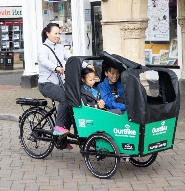 Woman cycling community cargo bike with two children