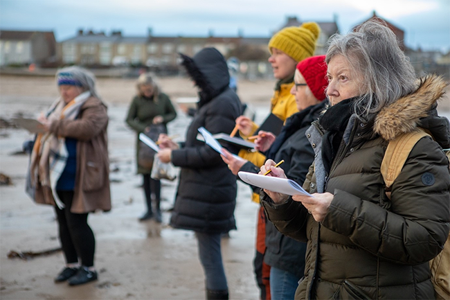 A group of people standing outside drawing on the beach