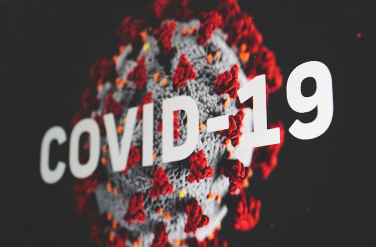 A coronavirus against a black backdrop with the copy COVID-19 in white in front of it