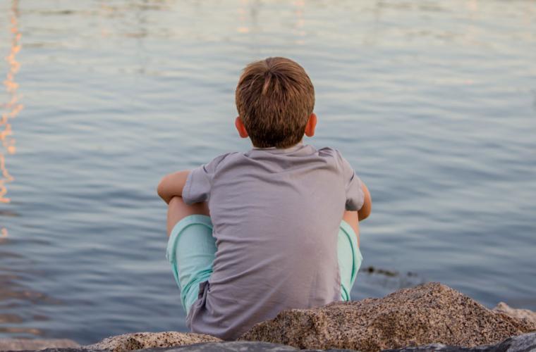photo of boy looking out onto a lake