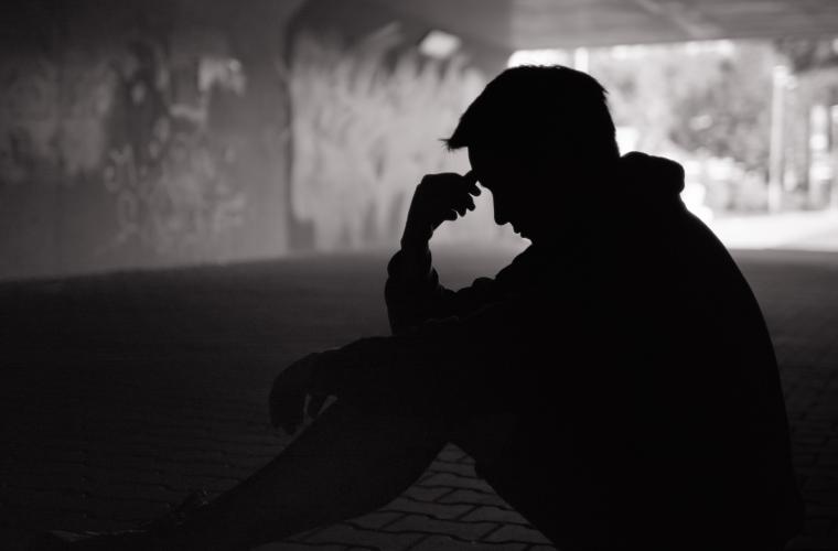 Homeless man sat down under a walk way with his head in his hands