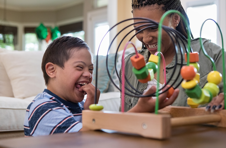 Young boy with down syndrome and his carer play with a toy