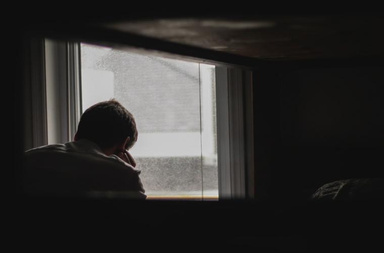Person in a darkened room looking outside a window