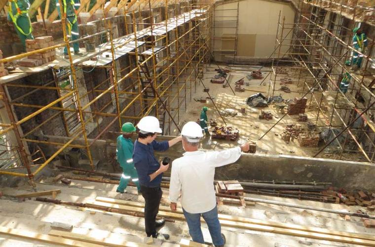 building site with builders and two men looking at plans in hard hats