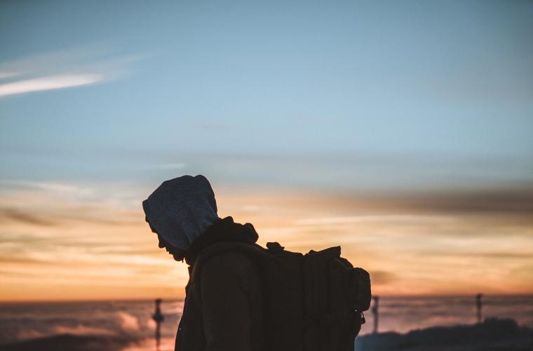 Man walking with hood up in the sun set looking down