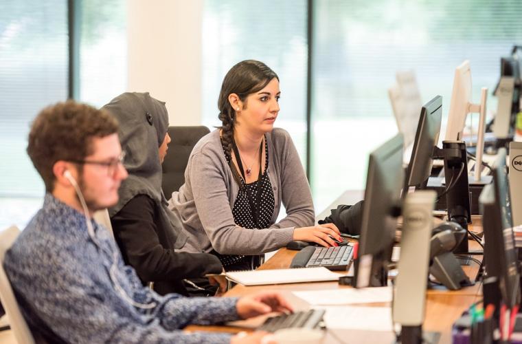 Two young women and one man sitting next to each other working on desktop computers in an office environment