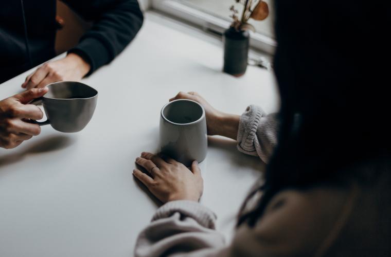Two people sat at a table both with cups of tea