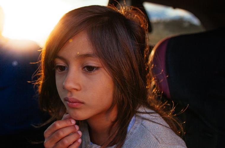 sad child deep in thought with sun reflection behind her
