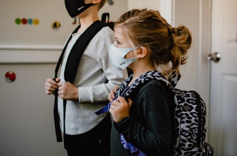 A boy and younger girl with backpacks and masks 941 x 627px
