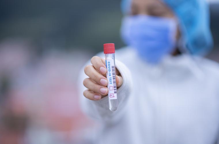 COVID tester holding out a vial with a sample