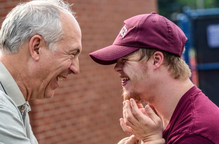 An older man and a younger man with down syndrome smiling at each other