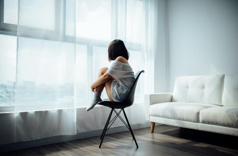 young woman sitting on a chair, wearing white, looking out of a window