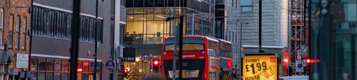 A busy city centre high street with a man walking down it. Bus is in the distance.