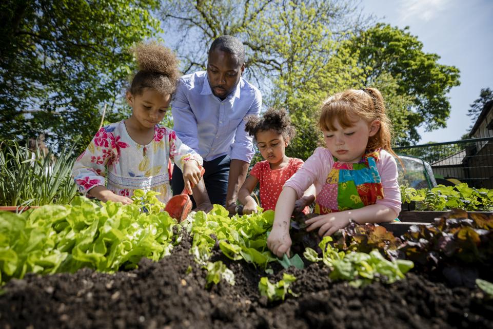 Adult with three children working in community garden